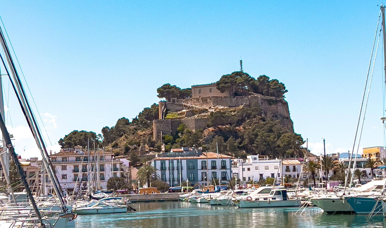 Blick auf die maurische Burg von Dénia über dem Yachthafen, umgeben von weißen Häusern und Segelbooten an der sonnigen Mittelmeerküste