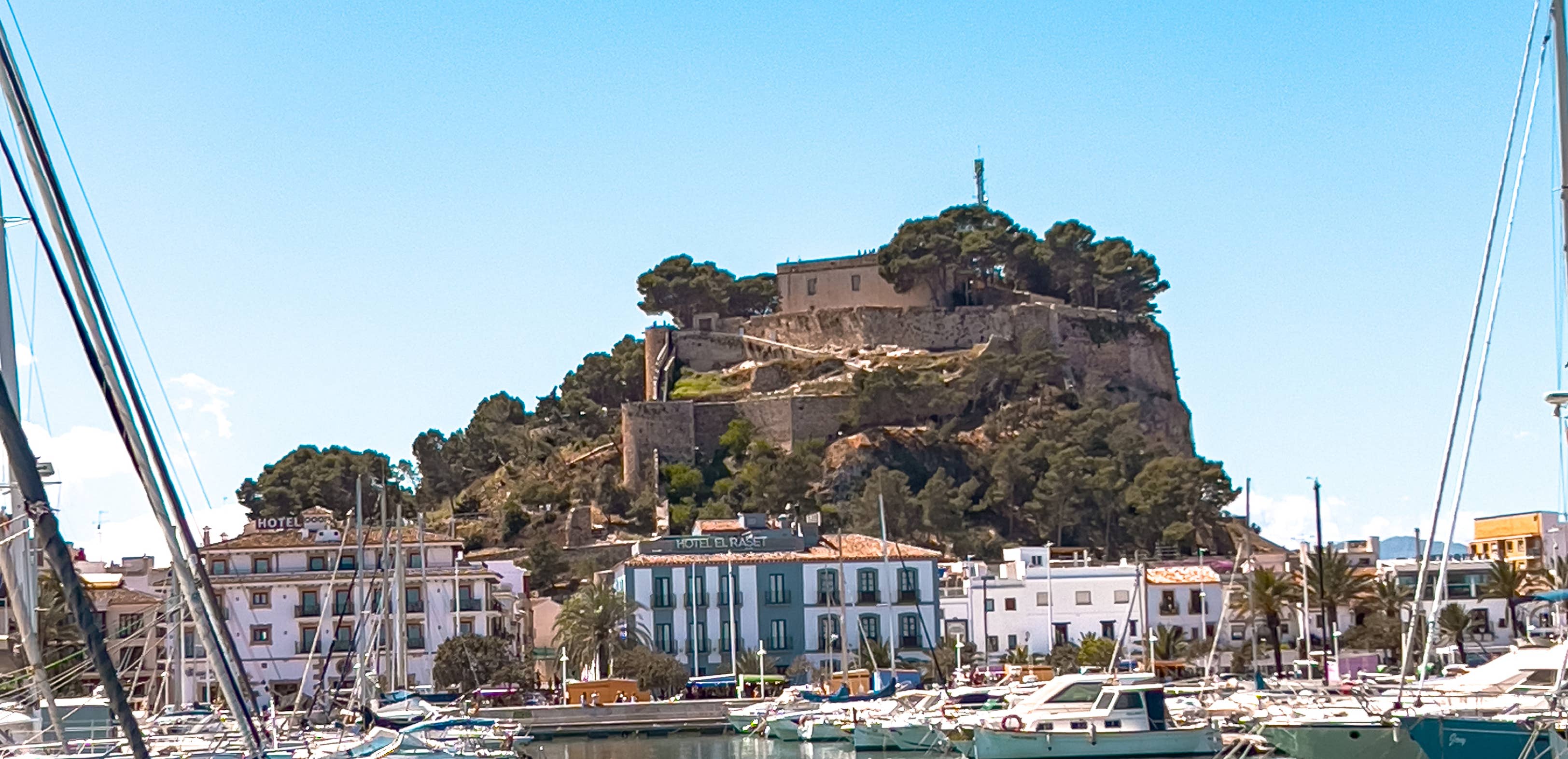 Blick auf die maurische Burg von Dénia über dem Yachthafen, umgeben von weißen Häusern und Segelbooten an der sonnigen Mittelmeerküste